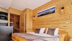 A wooden interior with a bed, a wooden wall with a picture, and a kitchen area.