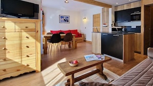 A modern living room with a wooden cabinet, a television, a dining area with a red sofa, and a kitchen with black cabinets and a black countertop.