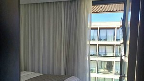 A bedroom with a large bed, a view of a building through a glass door, and a ceiling with a smoke detector. - Porto Alto Resort - GAV Resorts (NEAR PORTO DE GALINHA BEACH).  (Ipojuca)