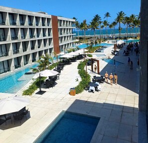 Ein Resort-Poolbereich mit mehreren Pools, Liegestühlen, Sonnenschirmen und Blick aufs Meer.