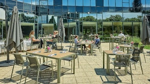 An outdoor patio area with tables and chairs, surrounded by a glass building reflecting the sky.
