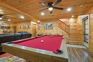 A wooden interior with a pool table, leather seating, and a staircase.