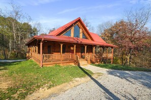 A log cabin with a red roof, a porch, and a gravel driveway.