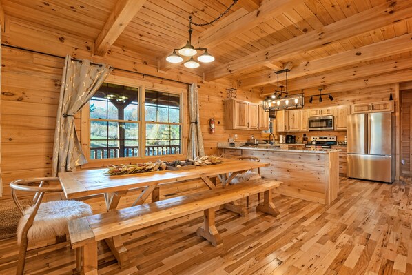 A wooden cabin interior with a dining table, benches, and a kitchen area featuring modern appliances.