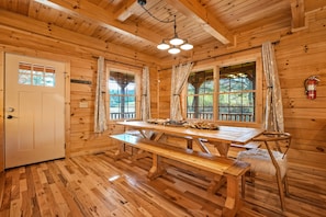 A wooden cabin interior with a large wooden table, benches, and a ceiling light fixture.