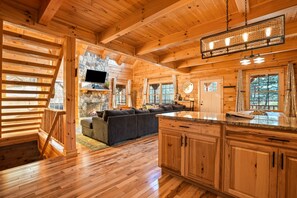 A wooden cabin interior with a living area, kitchen, and a stone fireplace.