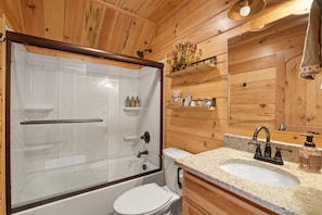 A wooden cabin bathroom with a glass-enclosed shower, a white toilet, and a sink with a granite countertop.
