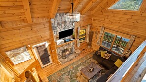 Een knus cabin interieur met een stenen open haard, een groot raam en een houten trap.