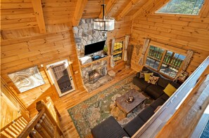 Een knus cabin interieur met een stenen open haard, een groot raam en een houten trap.