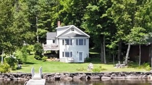 Une maison avec un quai s’avançant dans un lac paisible, entourée d’une végétation luxuriante.