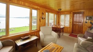 Une cabane en bois avec un coin repas, un fauteuil blanc et une vue sur un lac.