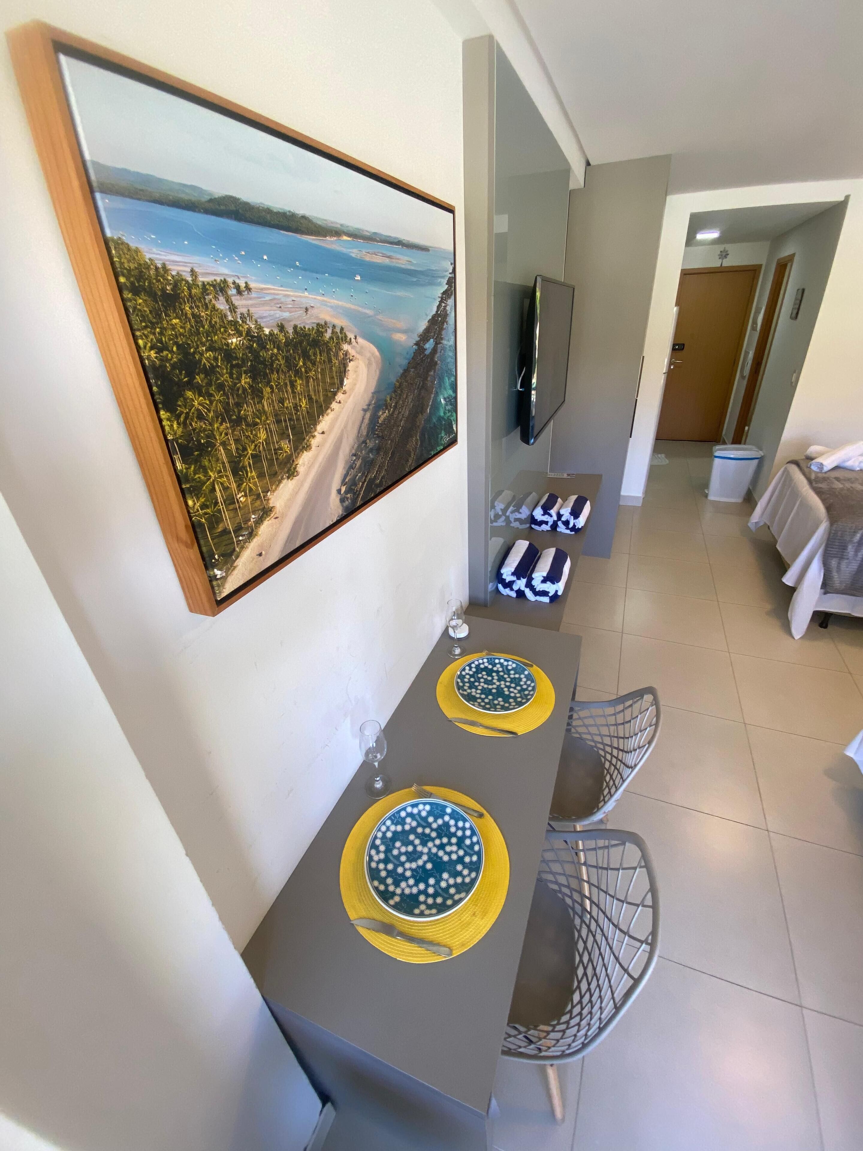 A dining area with a long table, two chairs, and a painting of a beach scene on the wall.
