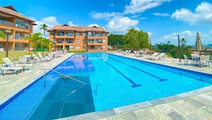 Ein Schwimmbecken mit Liegestühlen und Sonnenschirmen, umgeben von Gebäuden unter blauem Himmel.