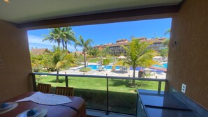 Ein Balkon mit Blick auf einen Pool und Palmen, ein Esstisch mit Tellern sowie eine Küchenzeile.