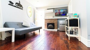 Ein Wohnzimmer mit grauem Sofa, einem weißen Couchtisch, einem Kamin und einem an der Wand befestigten Fernseher.