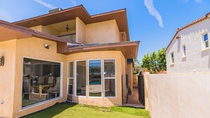 Ein zweistöckiges Haus mit einem großen Glasbalkon und Fenstern, einem kleinen Hinterhof und einem Nachbargebäude.