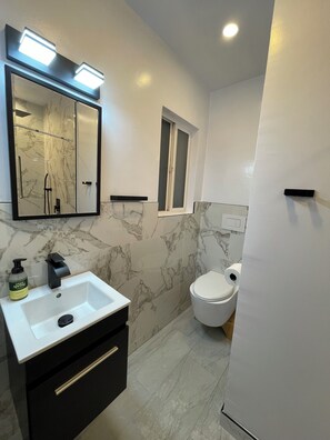 A modern bathroom with a marble backsplash, a white sink with a black faucet, a toilet, and a window above the toilet. - View Park with Private Pool (View Park-Windsor Hills)