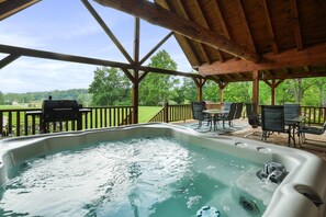 A hot tub under a wooden pergola with a view of a grassy field and trees.