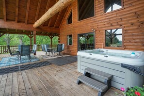 Een houten chalet met een jacuzzi, buitenmeubels en een overdekt terras.