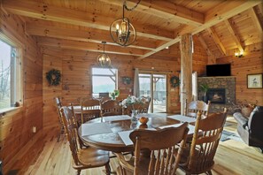 A wooden cabin interior with a dining table, chairs, a fireplace, and a stone fireplace surround. - MeadowLark Lodge | Hocking Hills, Sleeps 20, Views (Logan)