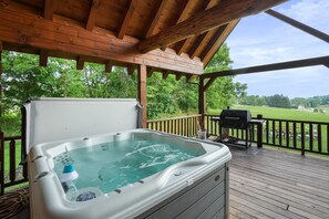 Een hottub op een houten terras, met uitzicht op een grasveld en bomen.