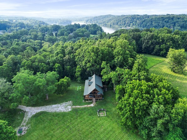 A cabin surrounded by dense forest, with a clear view of a lake in the background.