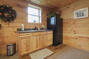 A wooden-paneled kitchen with a black refrigerator, wooden cabinets, a sink, and a window with a wreath.