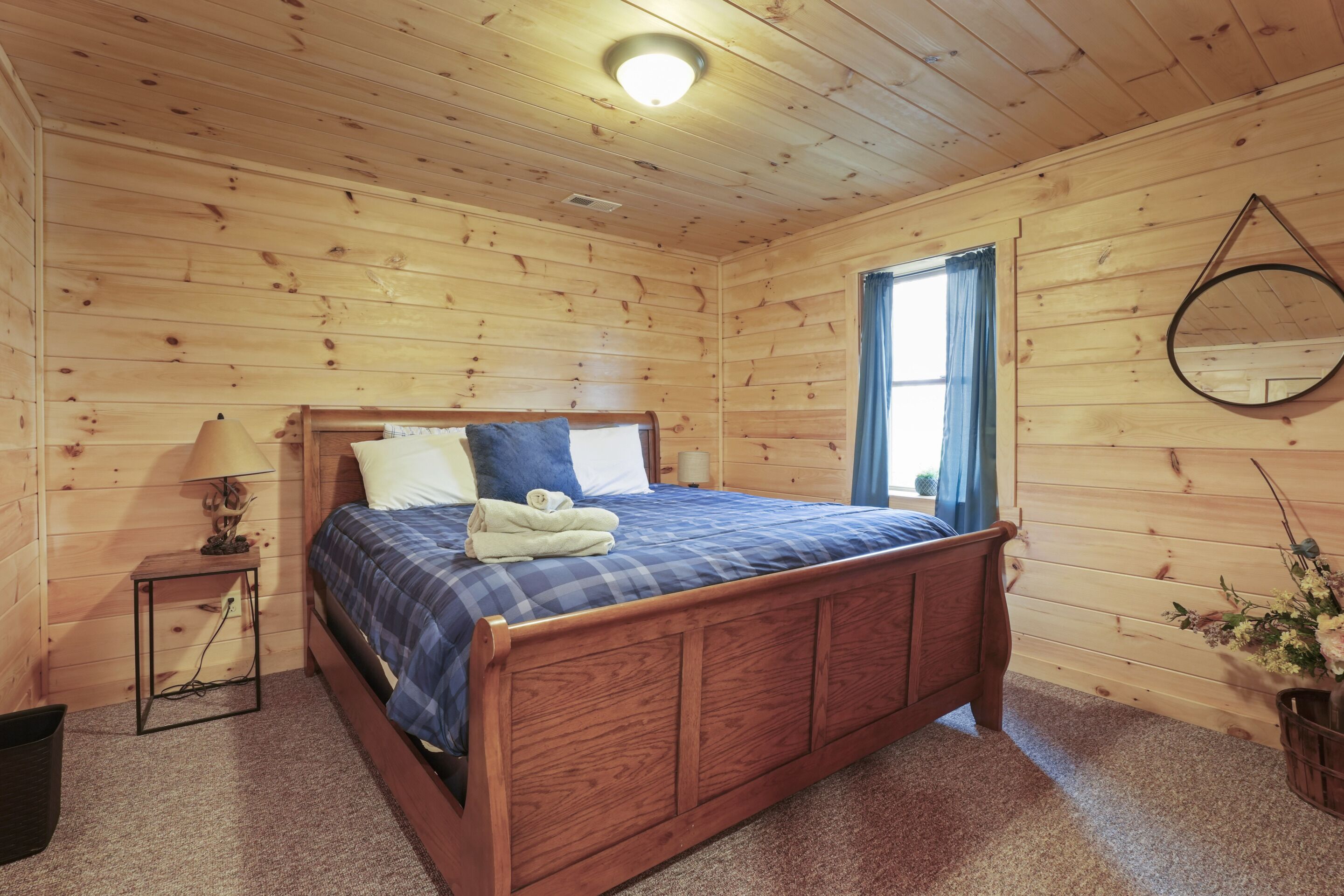 A wooden-paneled bedroom with a bed, a nightstand, a lamp, and a mirror.