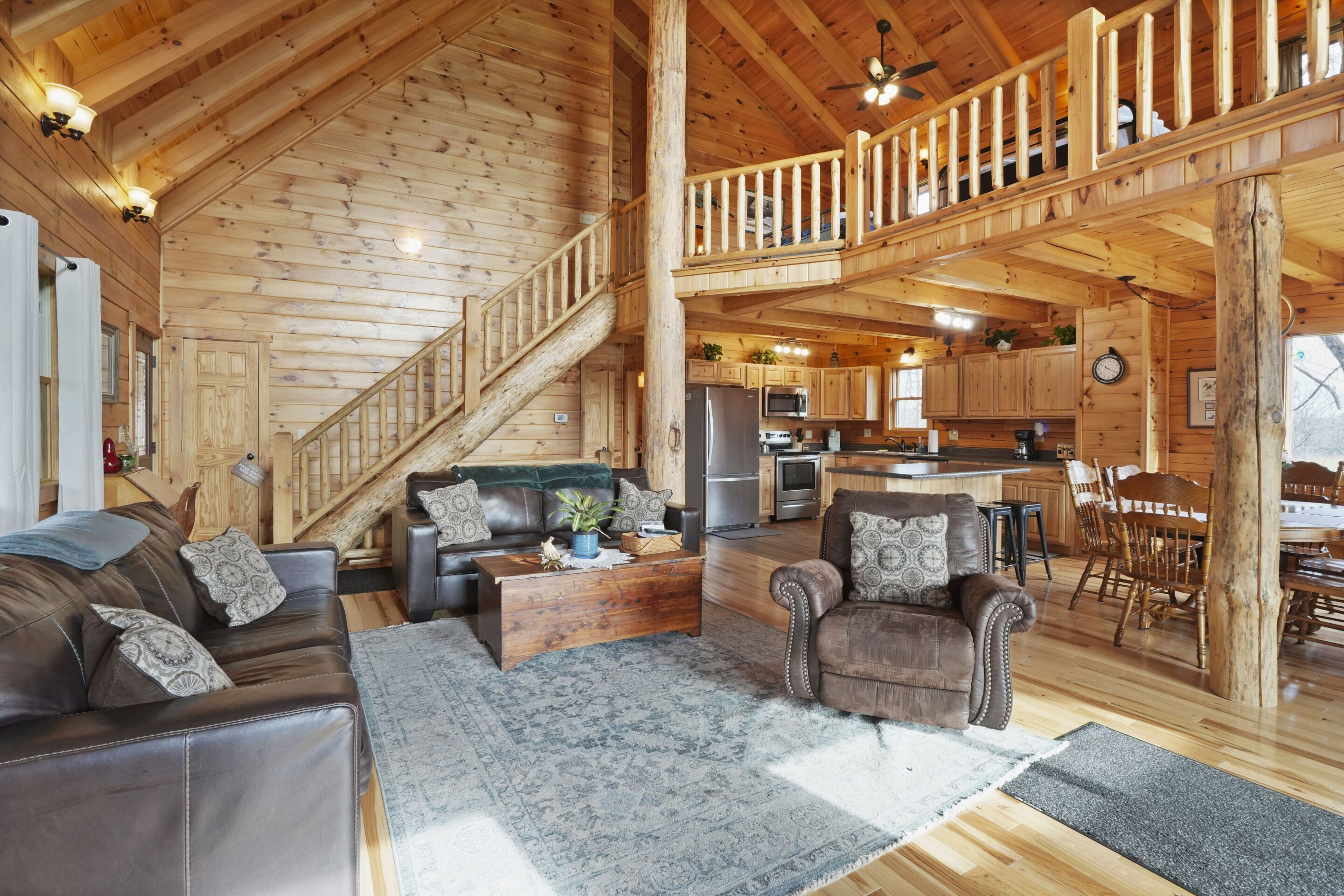 Una cabaña de madera espaciosa con habitación en el altillo, sala de estar con sofá y sillones, cocina con electrodomésticos modernos y comedor.