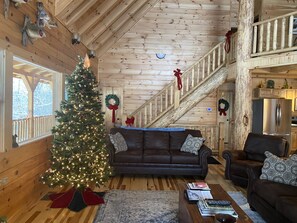 A cozy cabin interior with a Christmas tree, leather sofas, a staircase, and a kitchen area. - MeadowLark Lodge | Hocking Hills, Sleeps 20, Views (Logan)