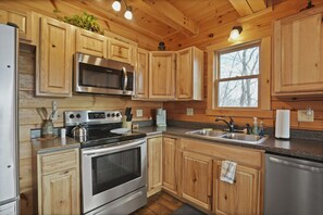 Een moderne keuken met houten kasten, roestvrijstalen apparatuur, een groot raam en een aanrecht met verschillende spullen.