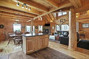 A spacious log cabin interior with a large dining area, kitchen, and living room.