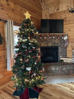 A Christmas tree with ornaments and lights, a stone fireplace, and a television mounted on the wall. - MeadowLark Lodge | Hocking Hills, Sleeps 20, Views (Logan)