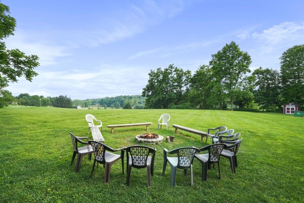 A circular seating arrangement with chairs and a fire pit in a grassy field.