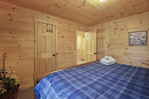A wooden-paneled room with a bed, a door, and a framed picture on the wall. - MeadowLark Lodge | Hocking Hills, Sleeps 20, Views (Logan)
