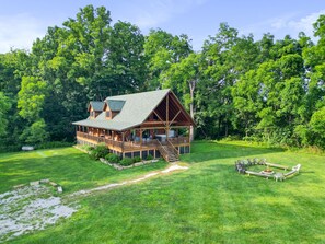 A wooden cabin with a deck, surrounded by lush greenery and trees.
