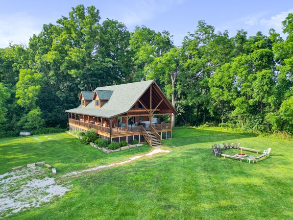 A wooden cabin with a deck, surrounded by lush greenery and trees.