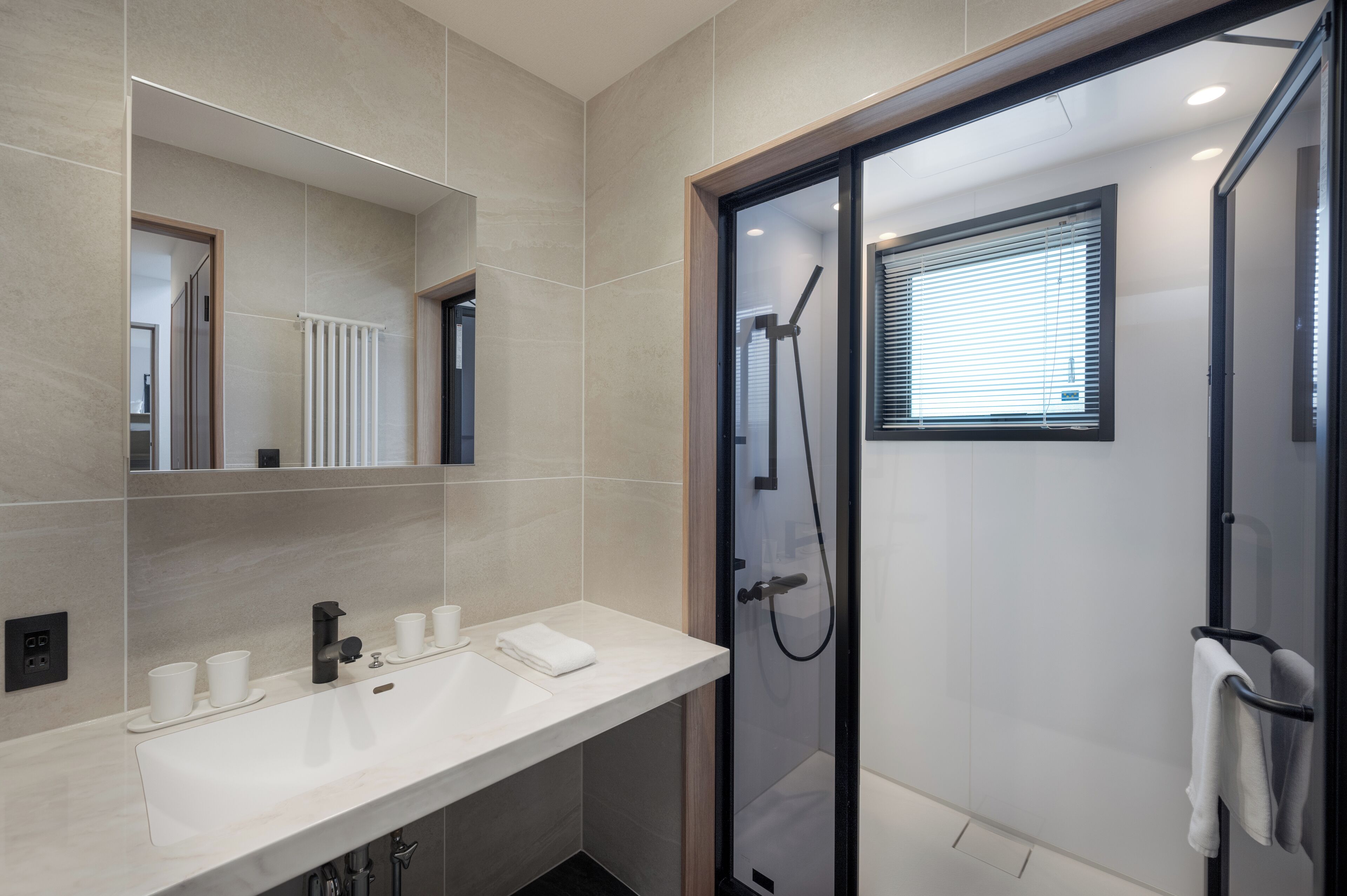 A modern bathroom with a glass shower enclosure, a large mirror, and a white sink with cups and a towel.