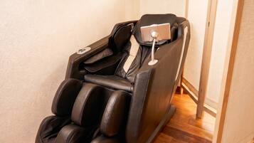 A massage chair with a control panel, positioned against a wall with wooden flooring.