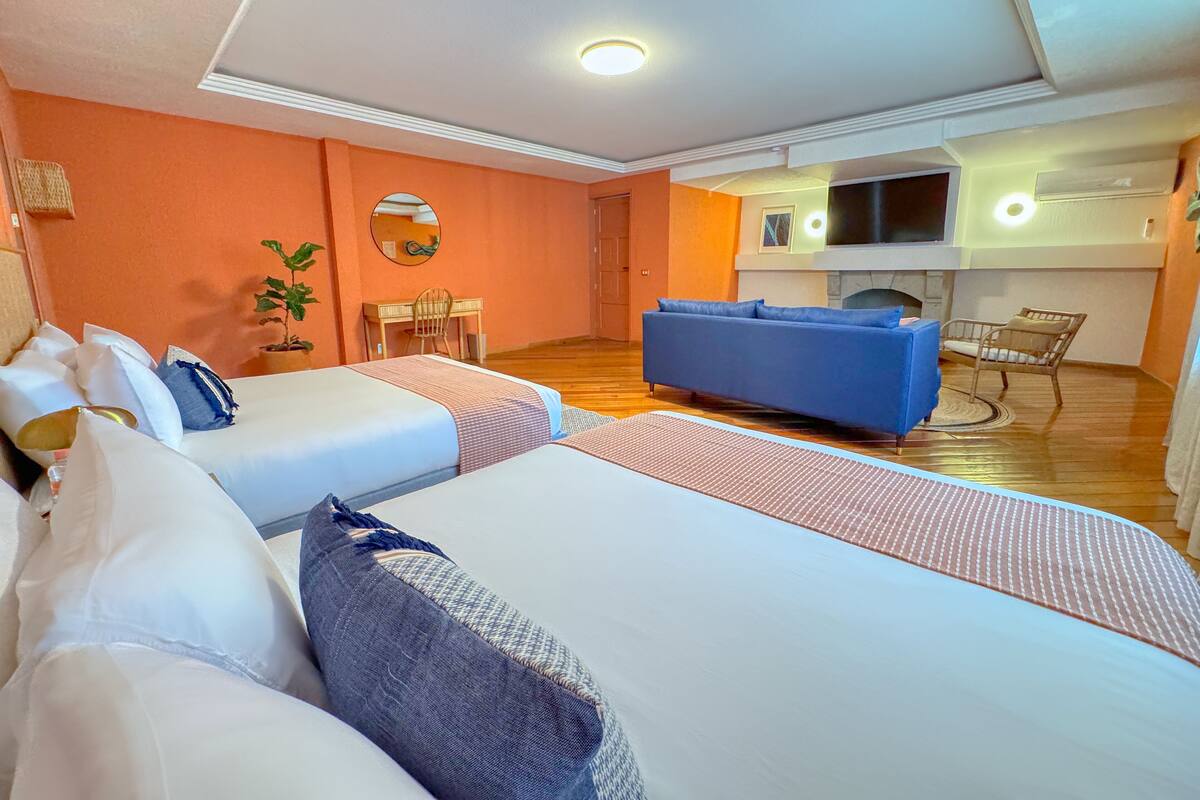 Une chambre d’hôtel avec deux lits, un canapé, une télévision et une cheminée.