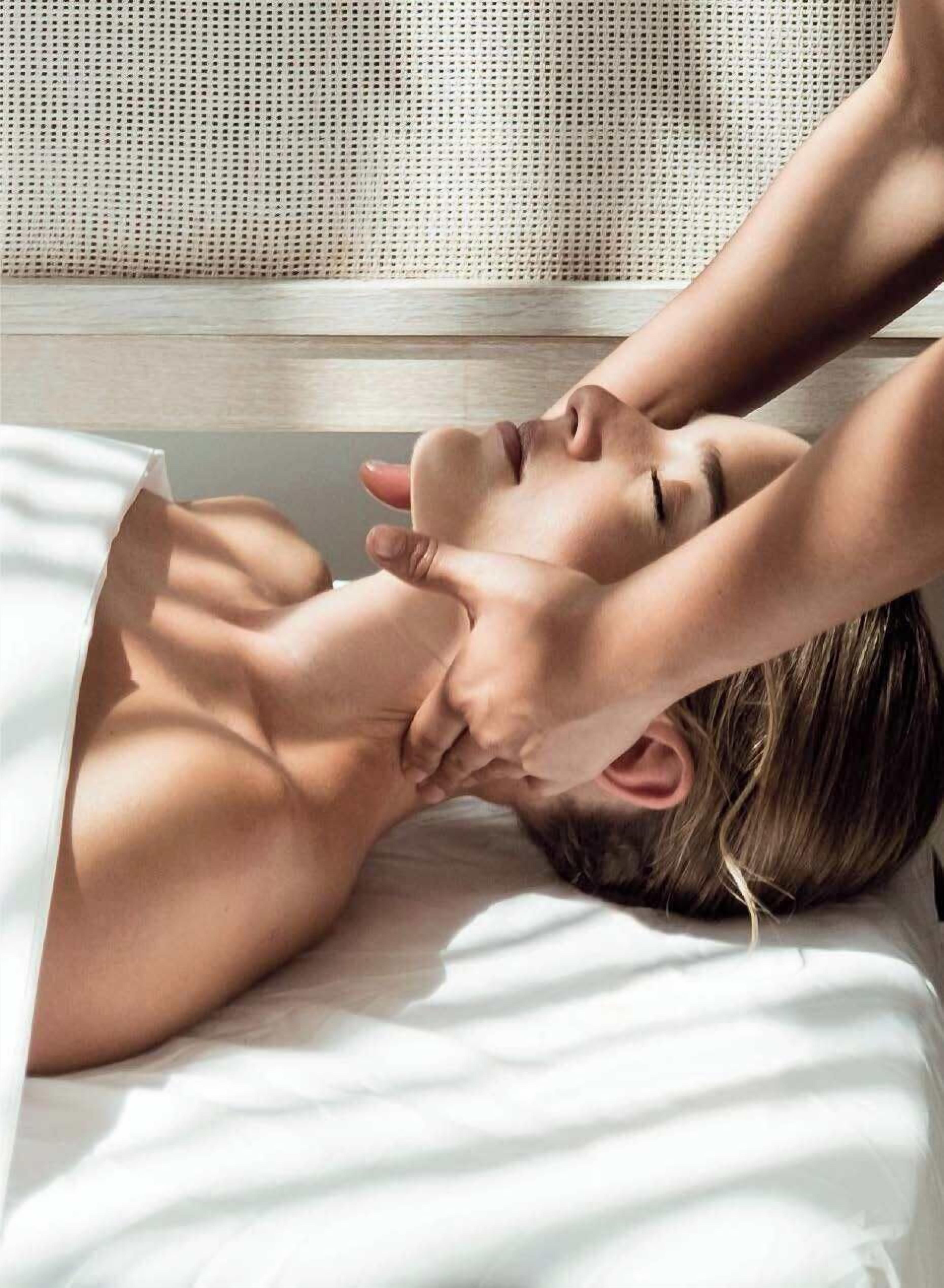 A person lying on a bed with a white sheet, receiving a massage.