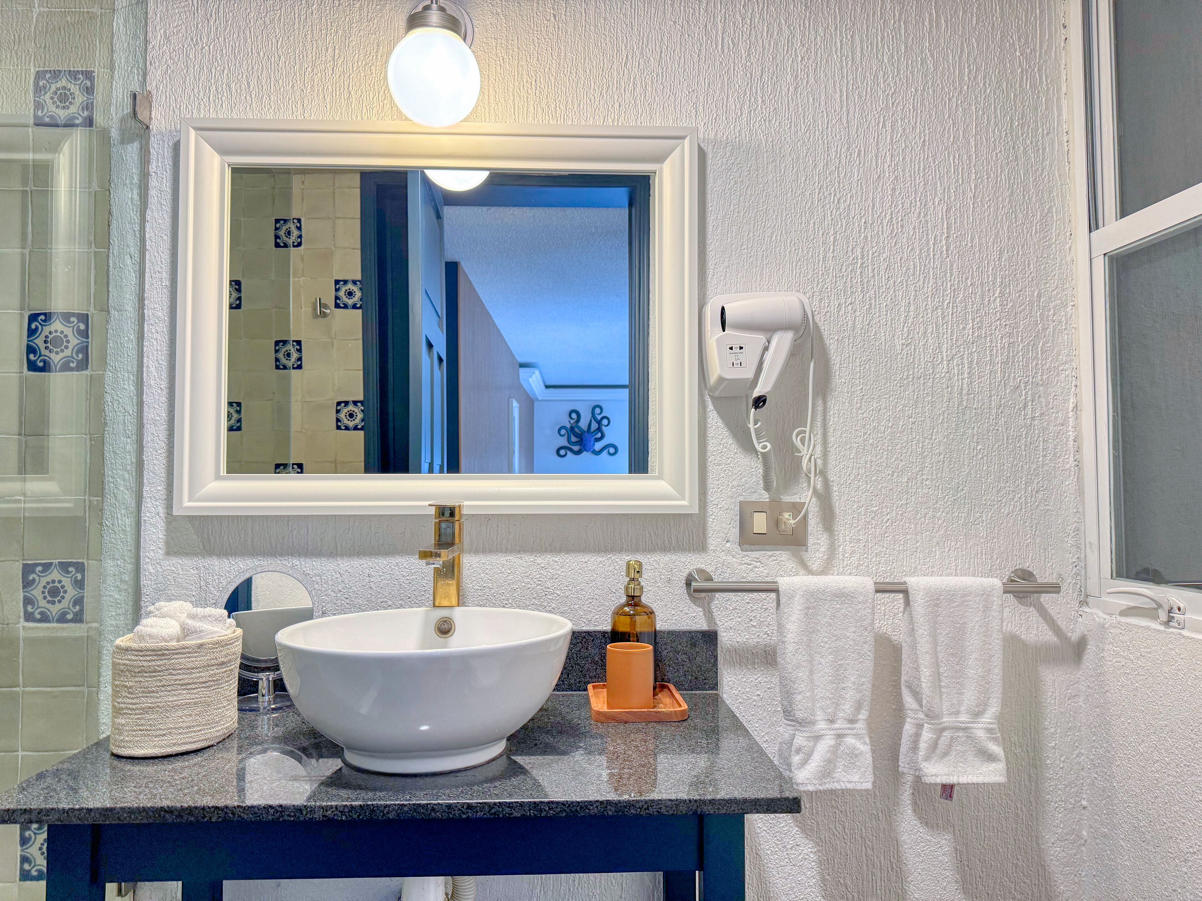 Ein Badezimmer mit einem weißen Waschbecken, einem Spiegel und einem Föhn an der Wand.