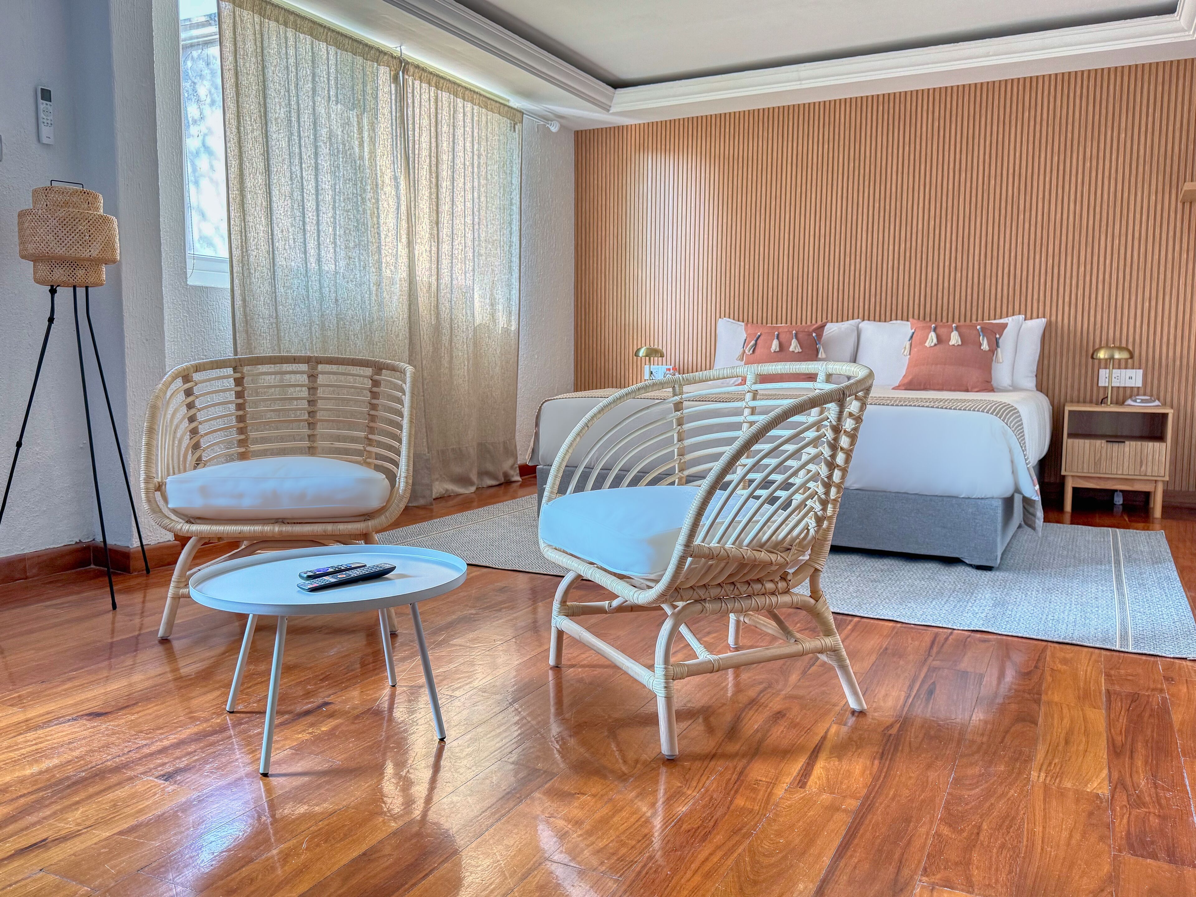 Een hotelkamer met een bed, twee rieten stoelen, een kleine tafel en een nachtkastje met een lamp.