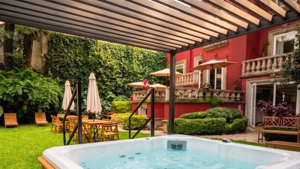 Un jacuzzi en un área exterior cubierta con mobiliario de madera y sombrillas.