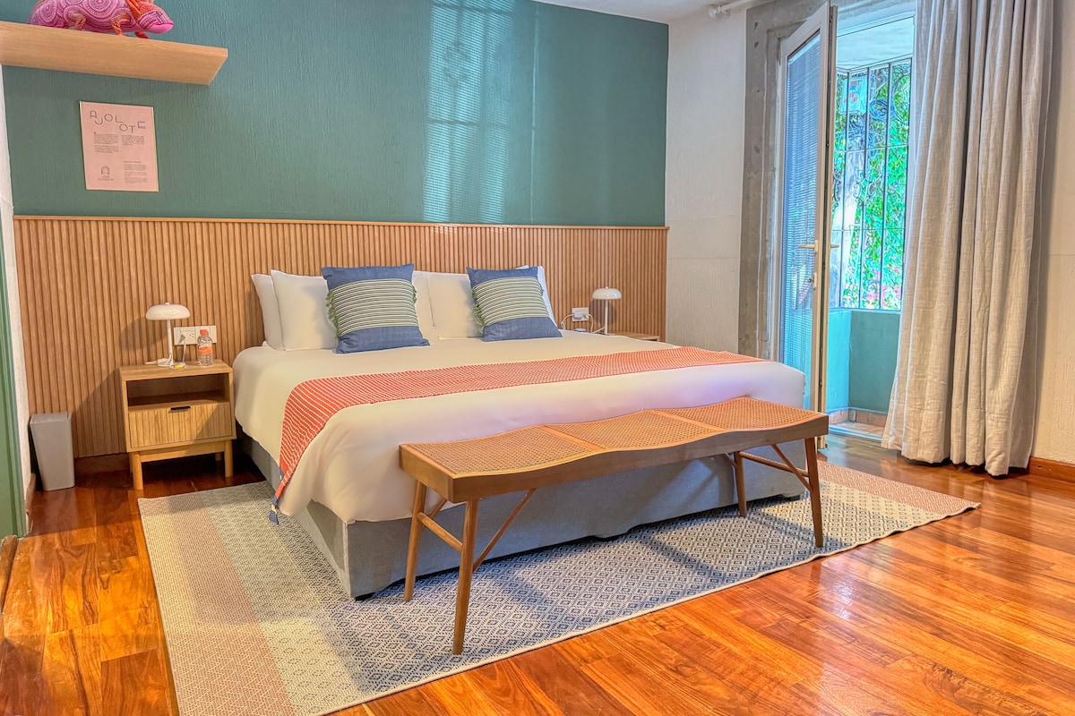A neatly arranged bedroom with a bed, bedside tables, a nightstand, a bench, and a window with curtains.
