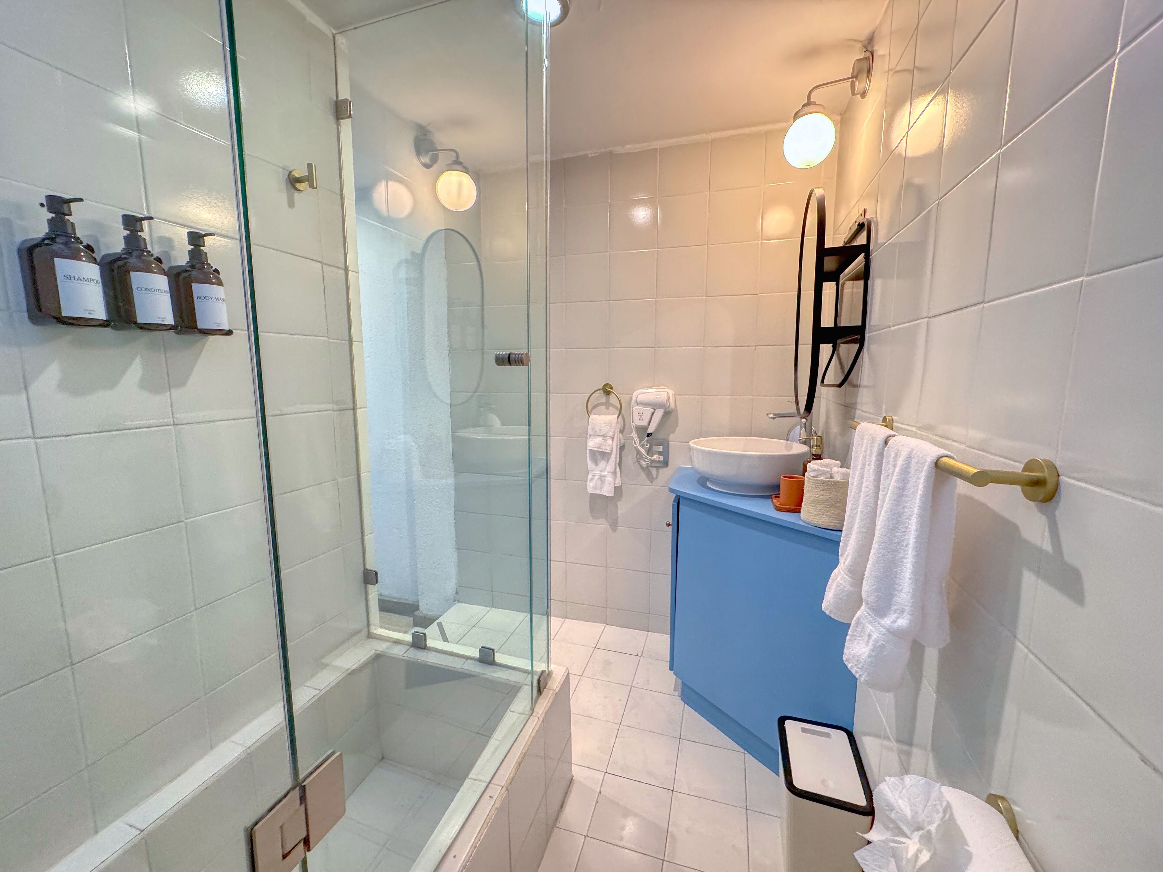 Et moderne badeværelse med et glasafskærmet brusebad, en hvid vask og en blå underskab.