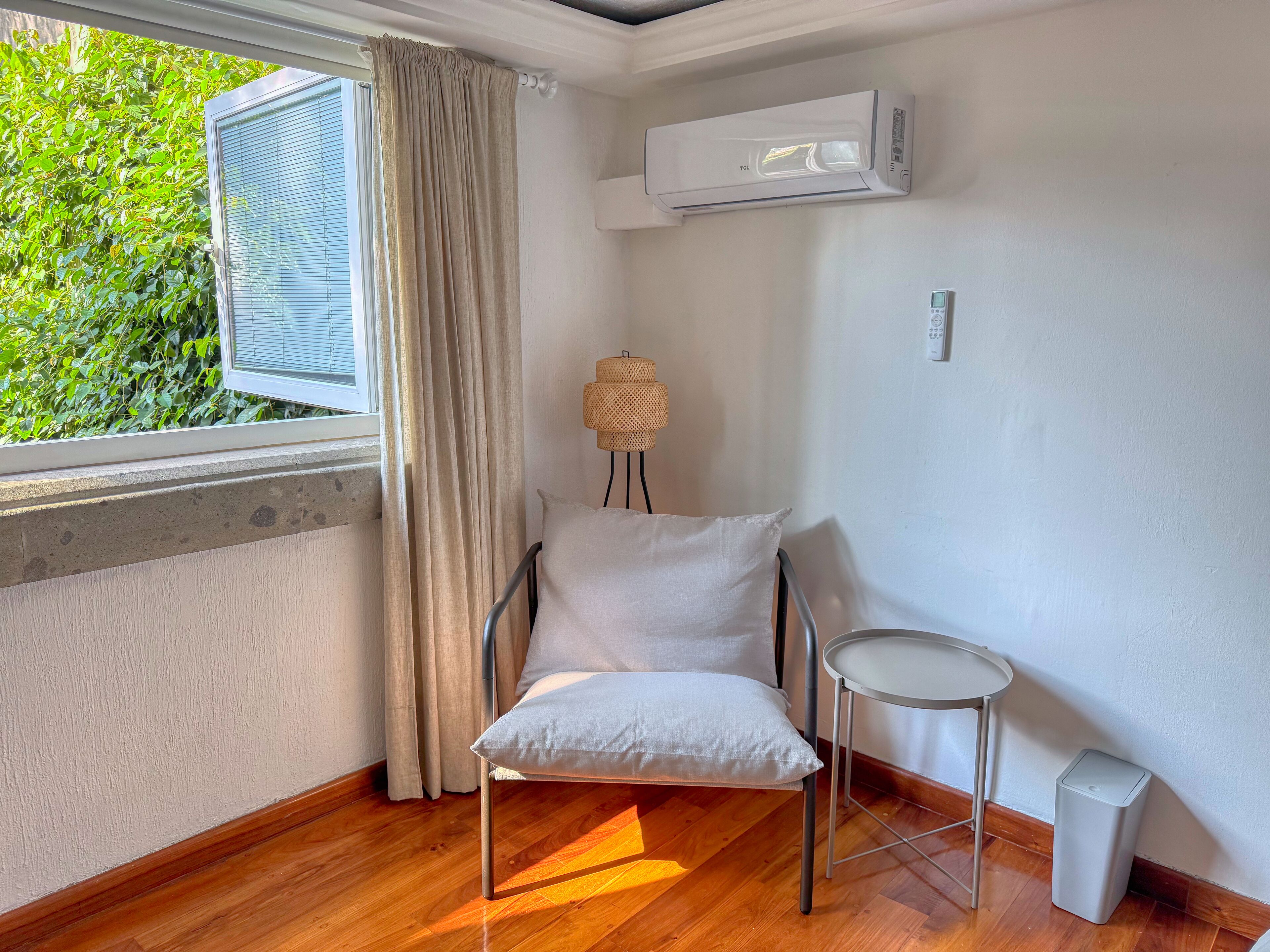 A room with a window, a chair, a small table, and an air conditioning unit.
