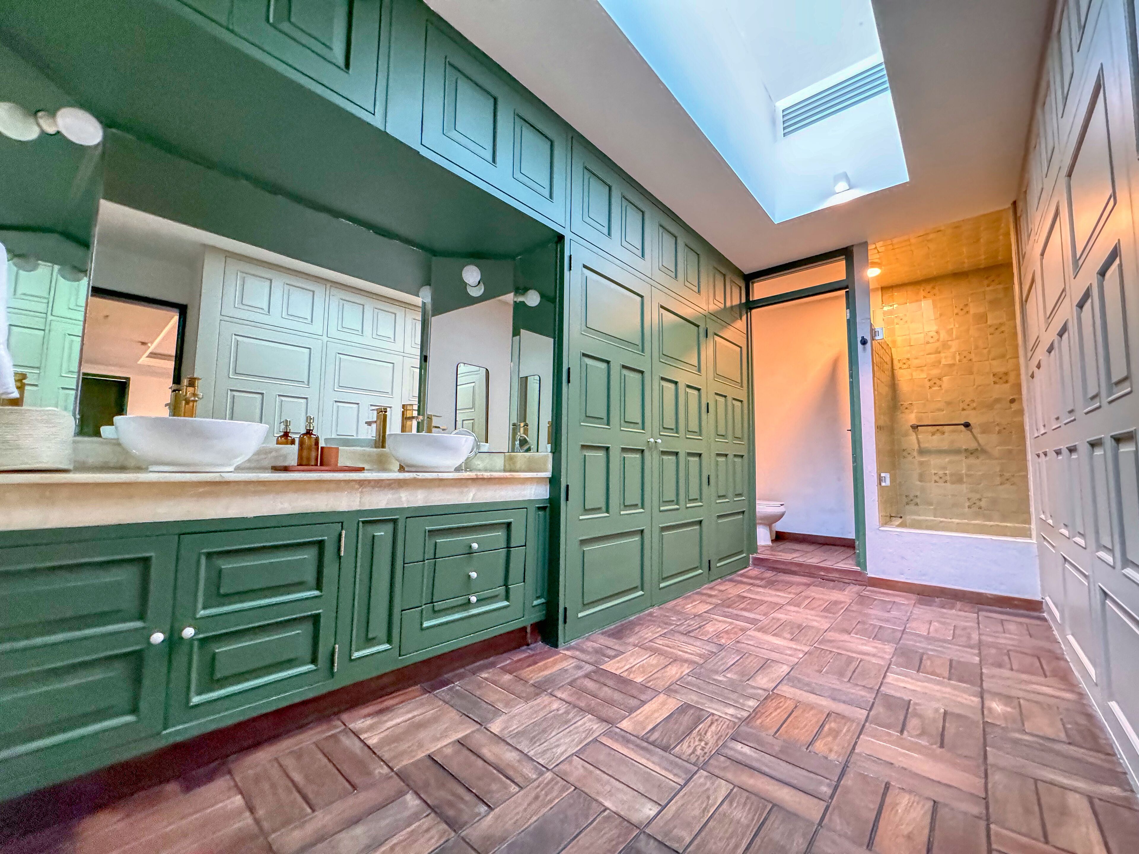 A modern bathroom with green cabinetry, a large mirror, and a skylight.