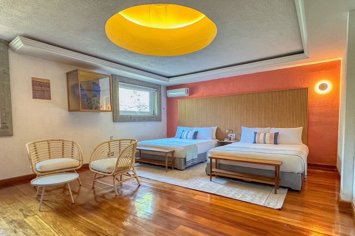 Une chambre d’hôtel avec deux lits, une grande fenêtre, des chaises en osier et un plancher en bois.