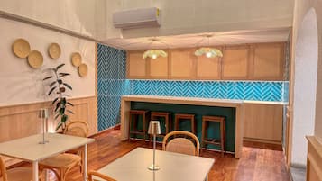 Interior de restaurante con suelo de madera, mesas redondas y sillas. Se observan placas decorativas en las paredes y un revestimiento de azulejos azules tipo espiga.